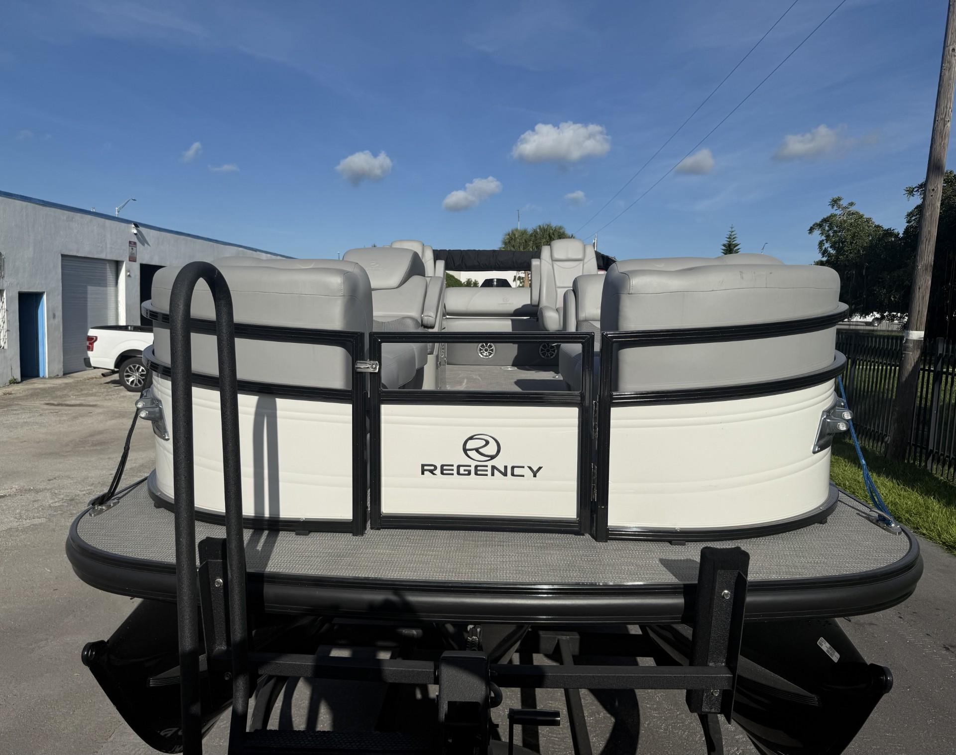 2024 Regency 250 DL3 pontoon boat, rear view, parked outdoors under a clear blue sky.