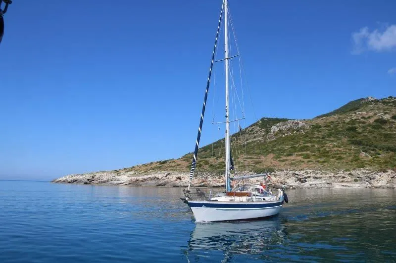  Yacht Photos Pics Sailboat Hallberg-Rassy 36 (1990) anchored near rocky coastline under clear blue sky.