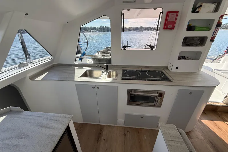  Yacht Photos Pics Modern kitchen interior of 2023 Schionning 1850 S catamaran with stove, sink, and window view.