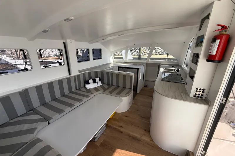  Yacht Photos Pics Modern interior of 2023 Schionning 1850 S catamaran with striped seating and kitchenette.