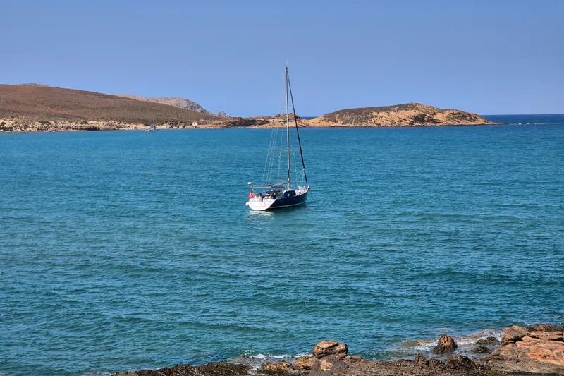 Pac Man Yacht Photos Pics Sailboat Beneteau Oceanis Clipper 473, 2001, anchored in serene blue waters near rocky coastline.