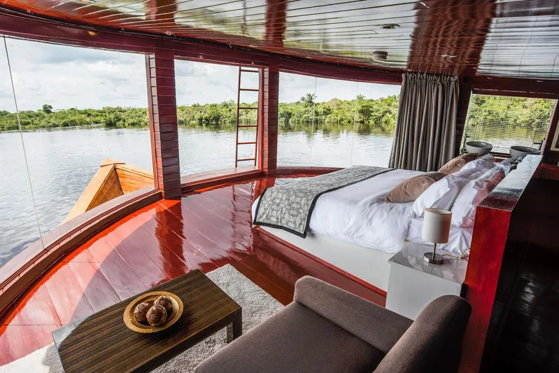 Crucero Amazonas Yacht Photos Pics Luxurious custom houseboat interior with panoramic river view, featuring a cozy bed and modern decor.