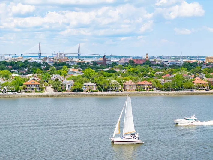 La Cura Yacht Photos Pics Sailboats on a serene river with a cityscape and bridge in the background.