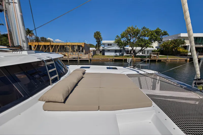 Lucky Dog Yacht Photos Pics 2022 Fountaine Pajot Tanna 47 catamaran with sunbathing area, docked near waterfront homes.
