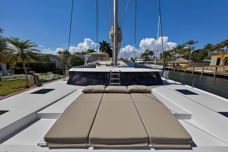 Lucky Dog Yacht Photos Pics 2022 Fountaine Pajot Tanna 47 catamaran with sunbathing area, docked by palm trees.