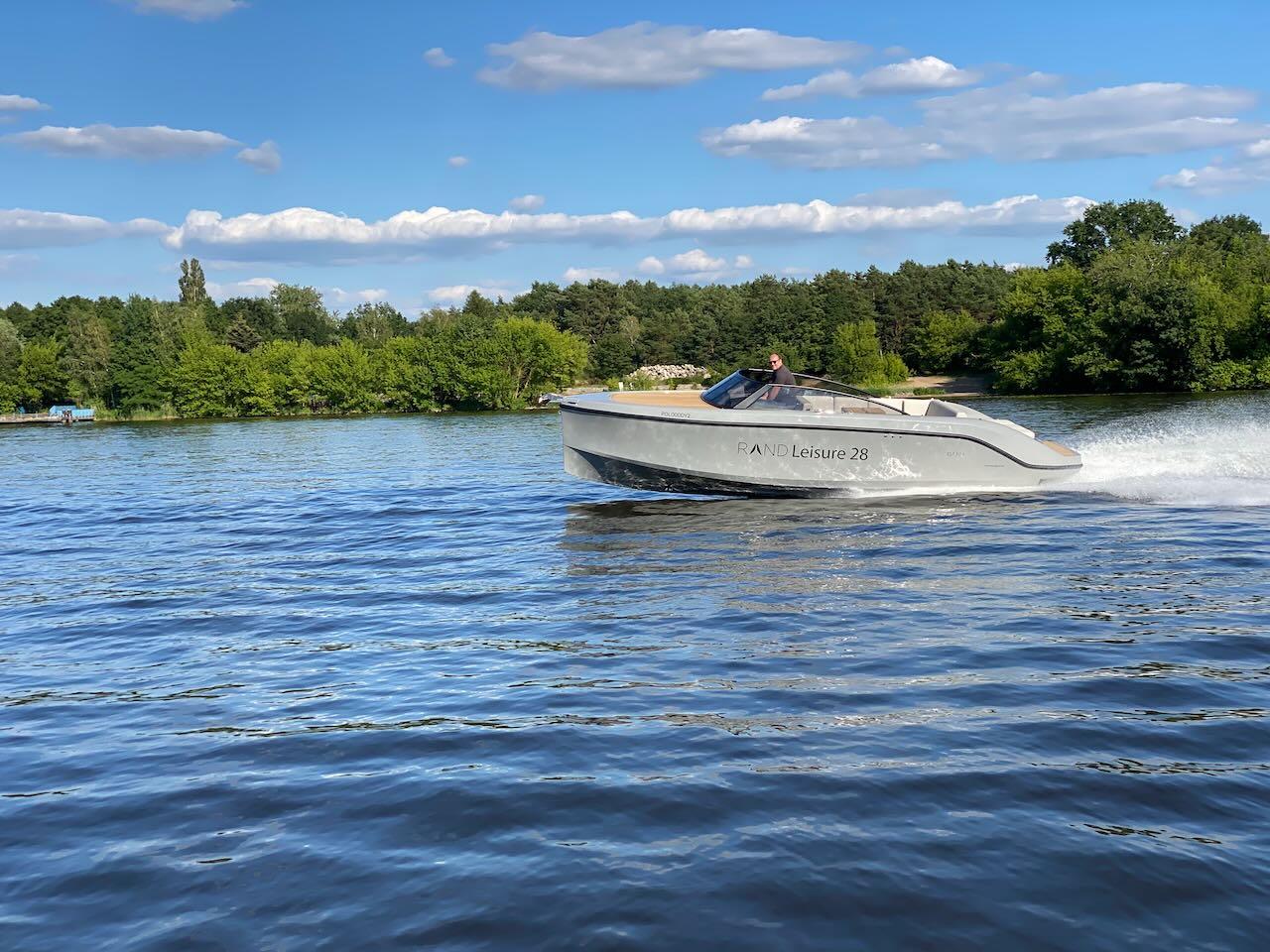2021 Rand Leisure 28 boat cruising on a serene lake with lush greenery.