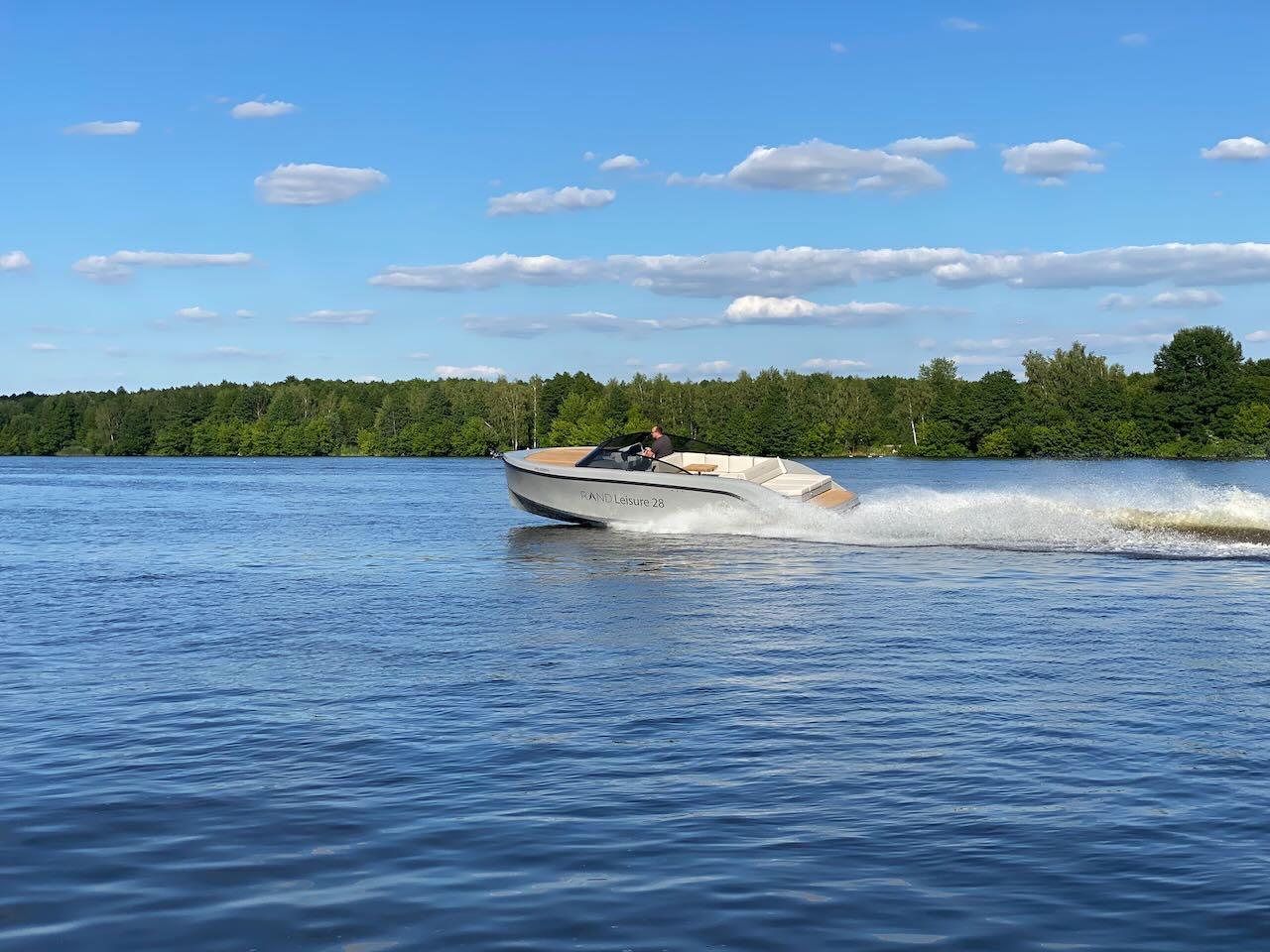 2021 Rand Leisure 28 boat cruising on a lake with a forested shoreline.