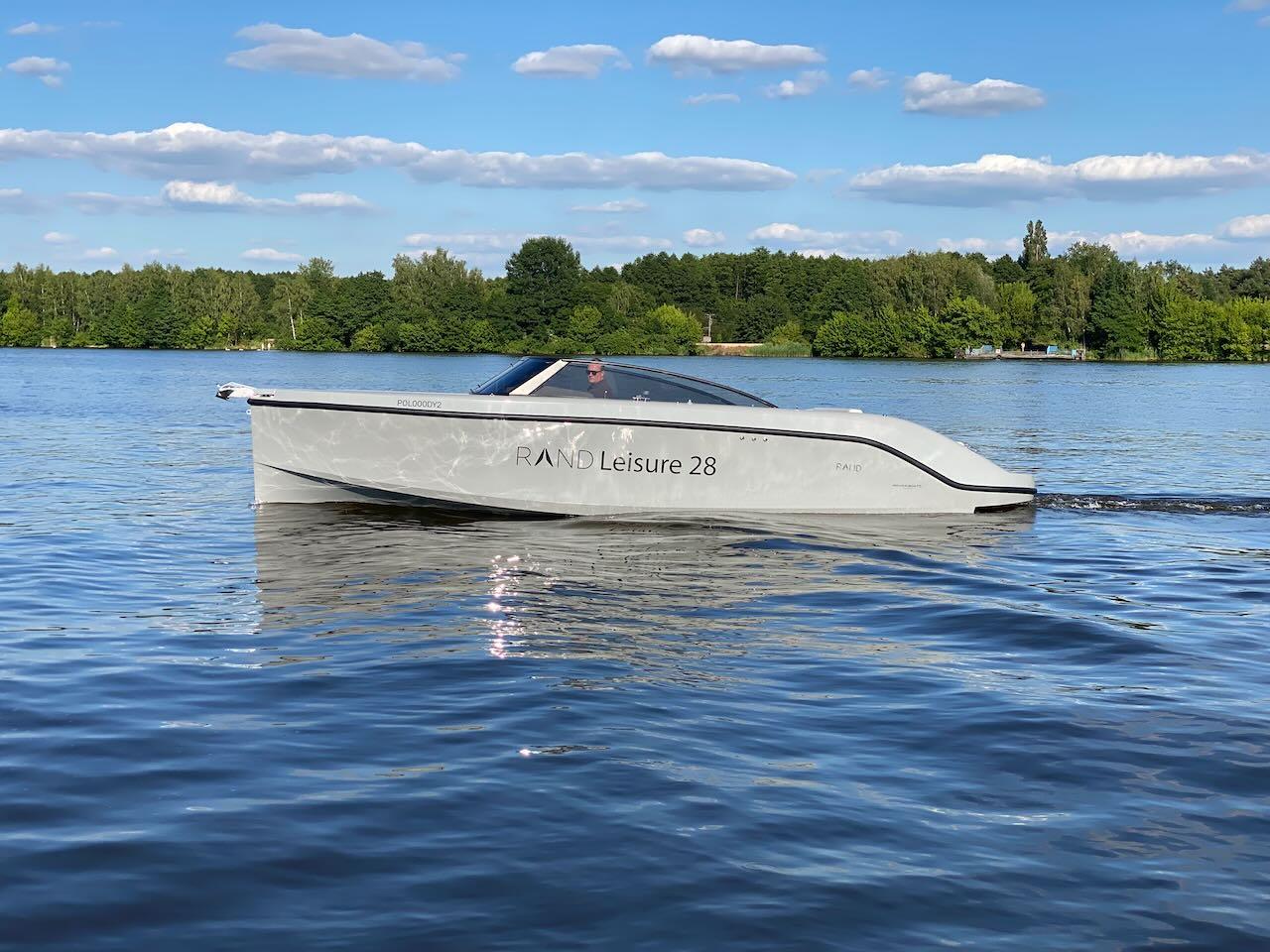 2021 Rand Leisure 28 boat cruising on a serene lake with lush green trees in the background.