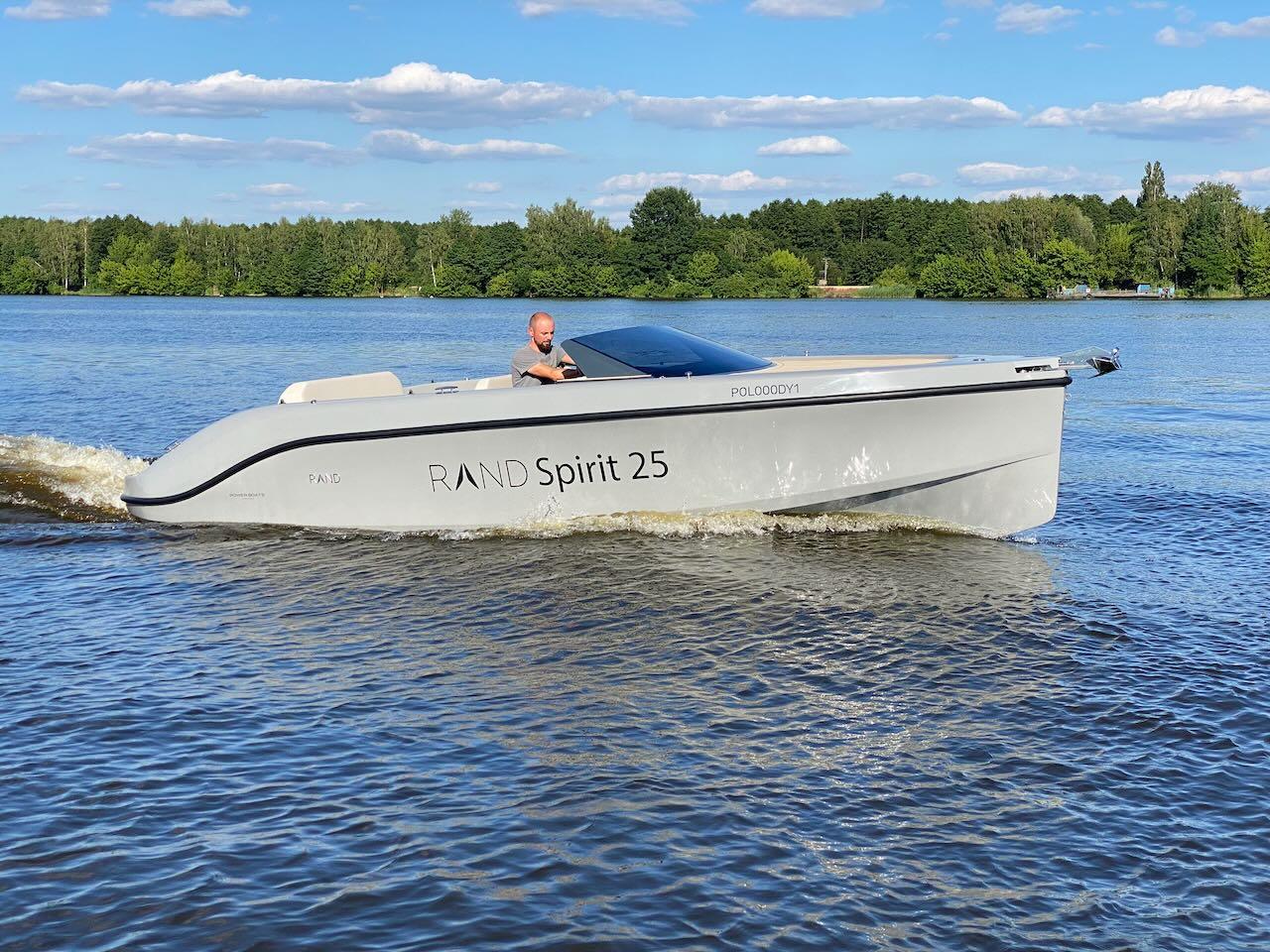 2022 Rand Spirit 25 boat cruising on a lake with a scenic forest background.