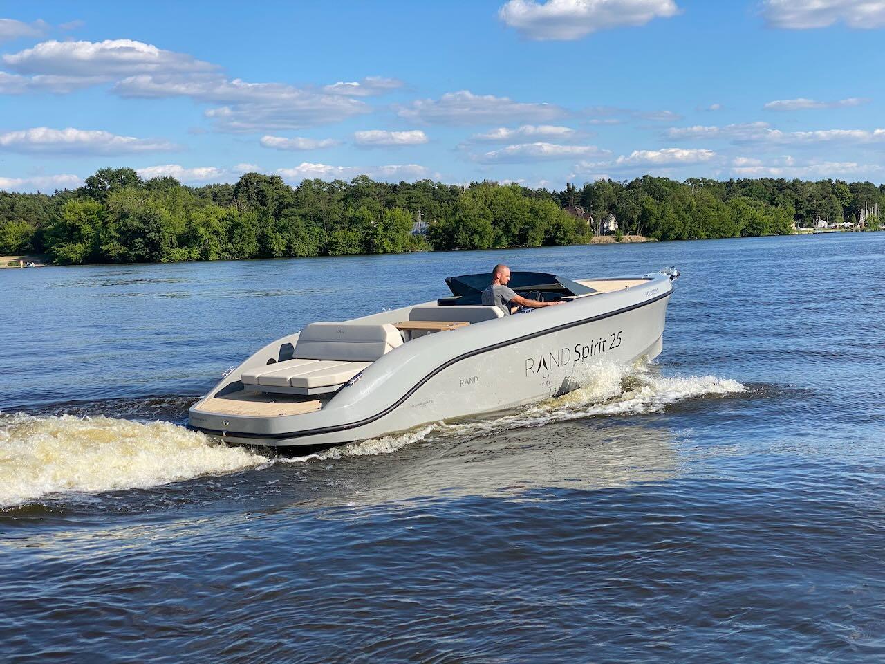 2022 Rand Spirit 25 boat cruising on a lake with lush green trees in the background.