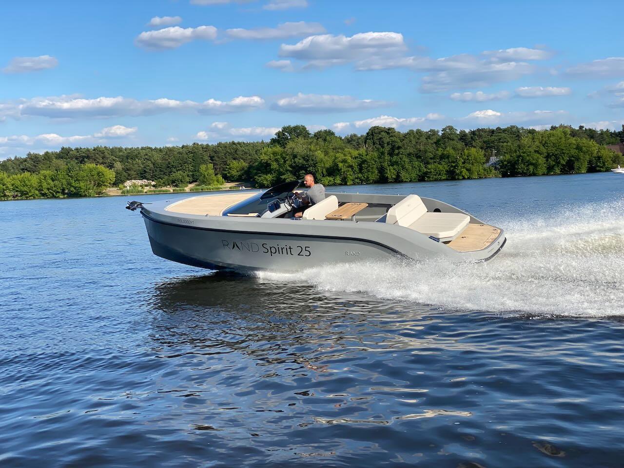 2022 Rand Spirit 25 boat cruising on a lake with scenic background.