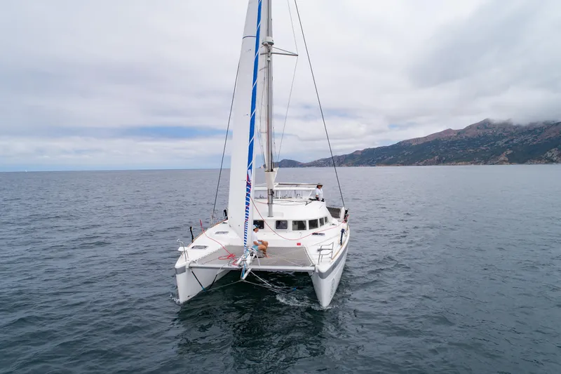 Seabatical Yacht Photos Pics 2016 Lagoon 380 catamaran sailing on open sea with mountainous coastline in background.