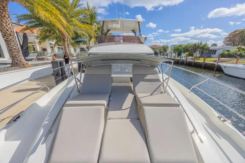 Happy Cay Yacht Photos Pics 2021 Prestige 520 Flybridge yacht with sun loungers, docked by palm trees and waterfront homes.