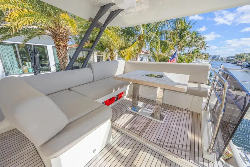 Happy Cay Yacht Photos Pics Luxurious 2021 Prestige 520 Flybridge yacht with elegant outdoor seating and table, surrounded by palm trees.