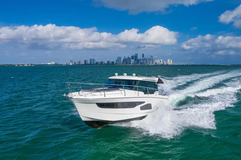  Yacht Photos Pics 2019 Jeanneau NC 1095 cruising on blue ocean with city skyline in background.