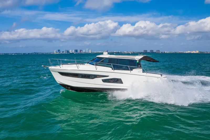  Yacht Photos Pics 2019 Jeanneau NC 1095 cruising on turquoise ocean with city skyline in background.
