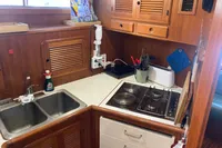 Compact kitchen in 1991 Trader 47 yacht with stove, sink, and wooden cabinetry.