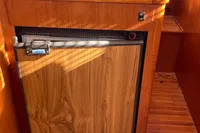 Wood-paneled mini fridge in 1991 Trader 47 boat interior with blue seat above.
