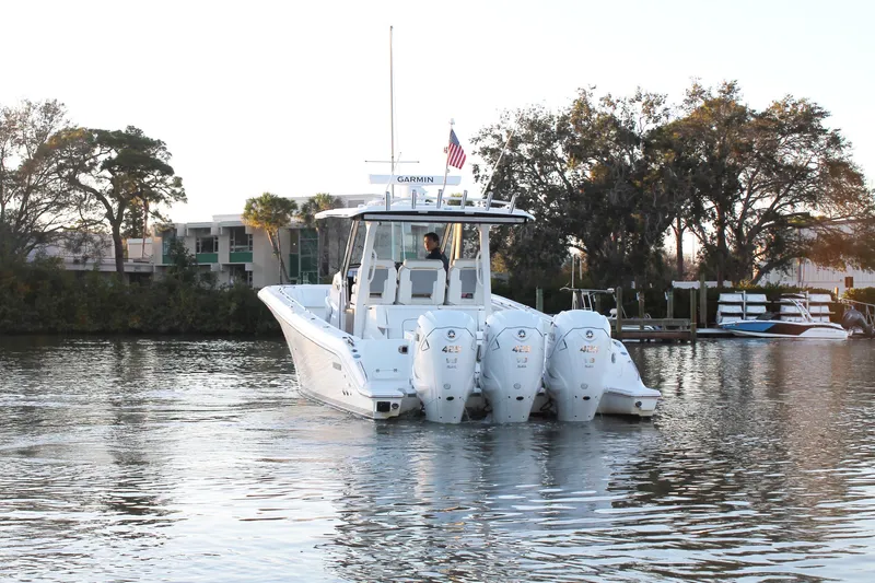  Yacht Photos Pics 2023 Pursuit S 378 Sport boat on calm water, surrounded by trees and docks.