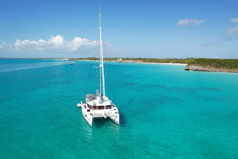 Khonsu Yacht Photos Pics 2023 Fountaine Pajot Isla catamaran sailing in clear turquoise waters near a tropical beach.