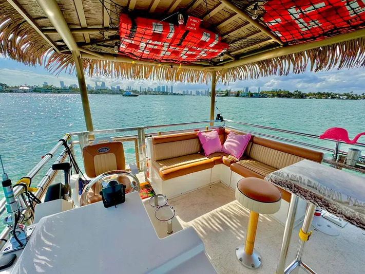 Tiki International Yacht Photos Pics Tropical-themed 2023 Beachcat 26 Tiki COI boat with seating, overlooking scenic waterfront.