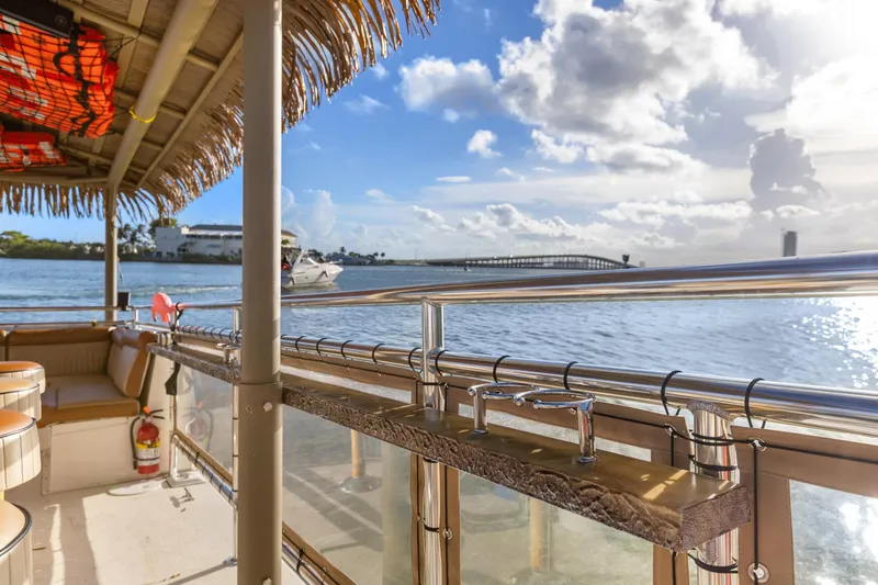 Tiki International Yacht Photos Pics Tropical-themed Beachcat 26 Tiki COI boat on serene water with bridge and cloudy sky.