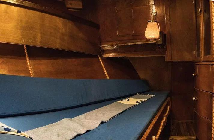  Yacht Photos Pics Interior of a 1981 Custom Traditional Motor Sailer, featuring wooden paneling and a cozy blue-cushioned berth.