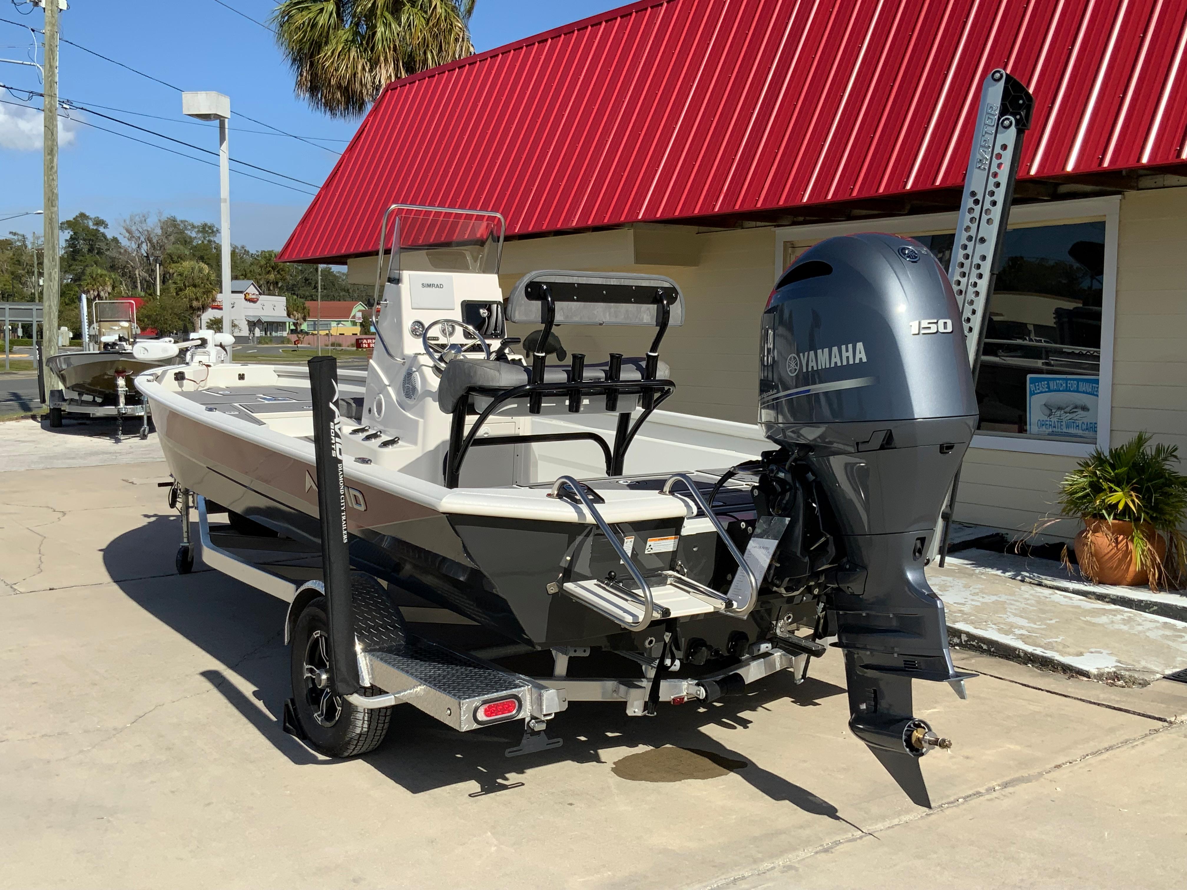 2023 Avid 21 Mag boat with Yamaha 150 engine outside a building with a red roof.