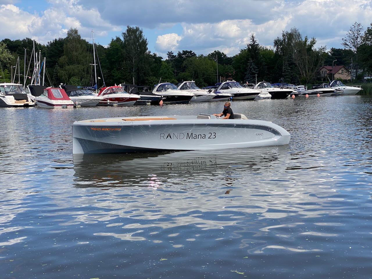 Modern Rand Mana 23 boat on a calm lake, surrounded by other boats.