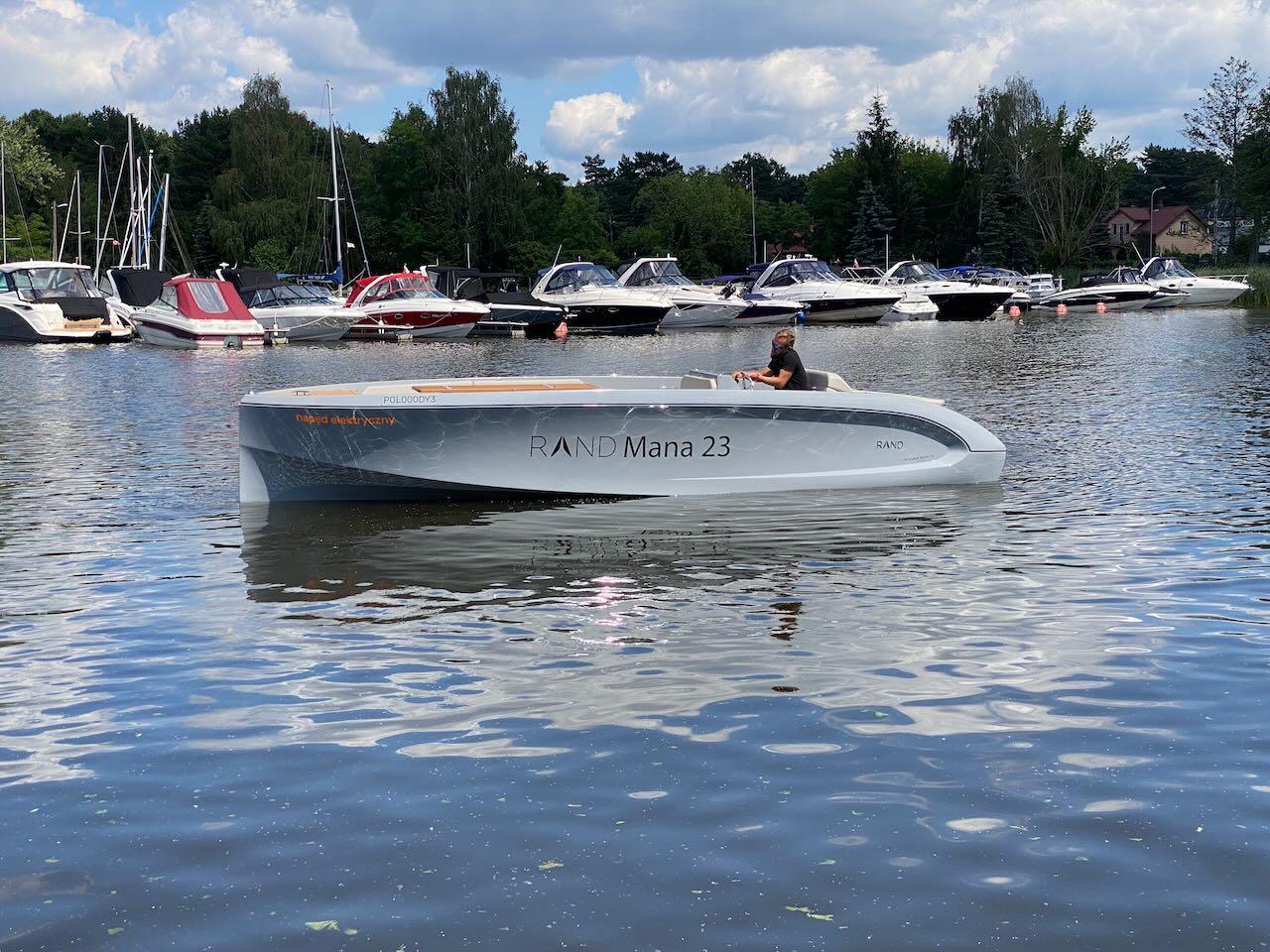 Modern Rand Mana 23 boat on a calm lake, surrounded by other boats.