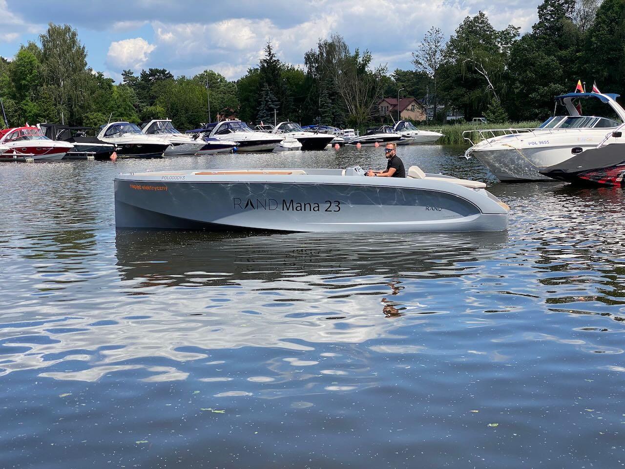 2021 Rand Mana 23 boat on a calm lake with other boats in the background.