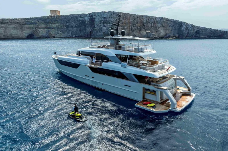 Unique S Yacht Photos Pics Luxury 2024 Sanlorenzo SD118 yacht cruising near rocky coastline, with person on jet ski nearby.