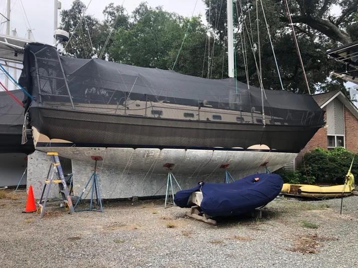 Otter II Yacht Photos Pics 1999 Island Packet 45 sailboat on stands, covered, with trees and a house in the background.