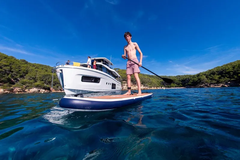  Yacht Photos Pics Young man paddleboarding near 2025 Beneteau Swift Trawler 54 in scenic coastal waters.