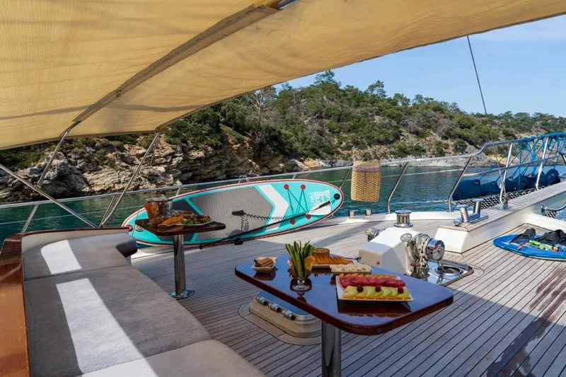  Yacht Photos Pics Luxurious 2022 Gulet 24m yacht deck with dining setup and paddleboard, scenic coastal view.
