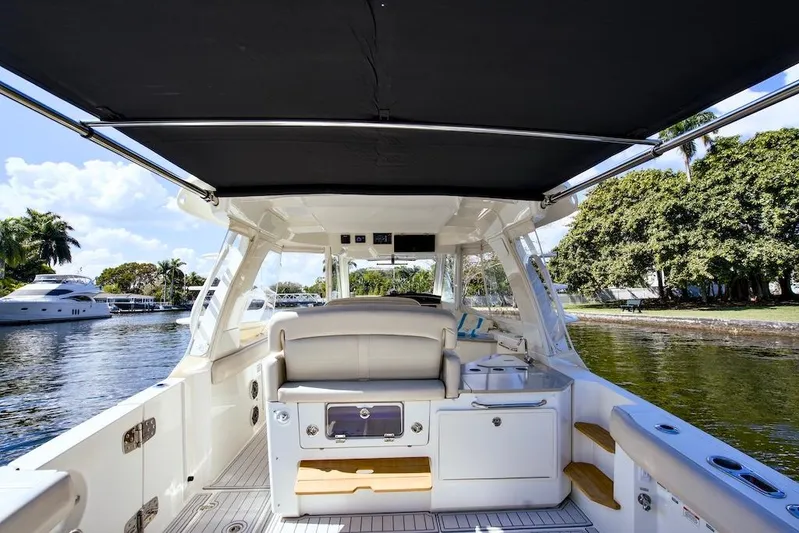 350 Realm Yacht Photos Pics 2019 Boston Whaler 350 Realm boat interior with canopy, docked near lush greenery.