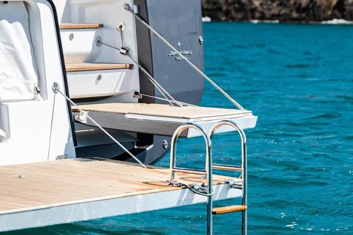 Yachting Conseil Yacht Photos Pics 2023 Jeanneau 60 yacht with swim platform and ladder on turquoise water.
