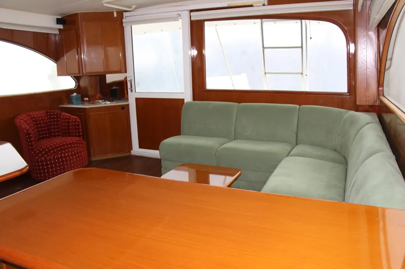 Galatea Yacht Photos Pics Luxurious yacht interior with green sectional sofa, wooden cabinetry, and red armchair, Post 50 model, 2000.