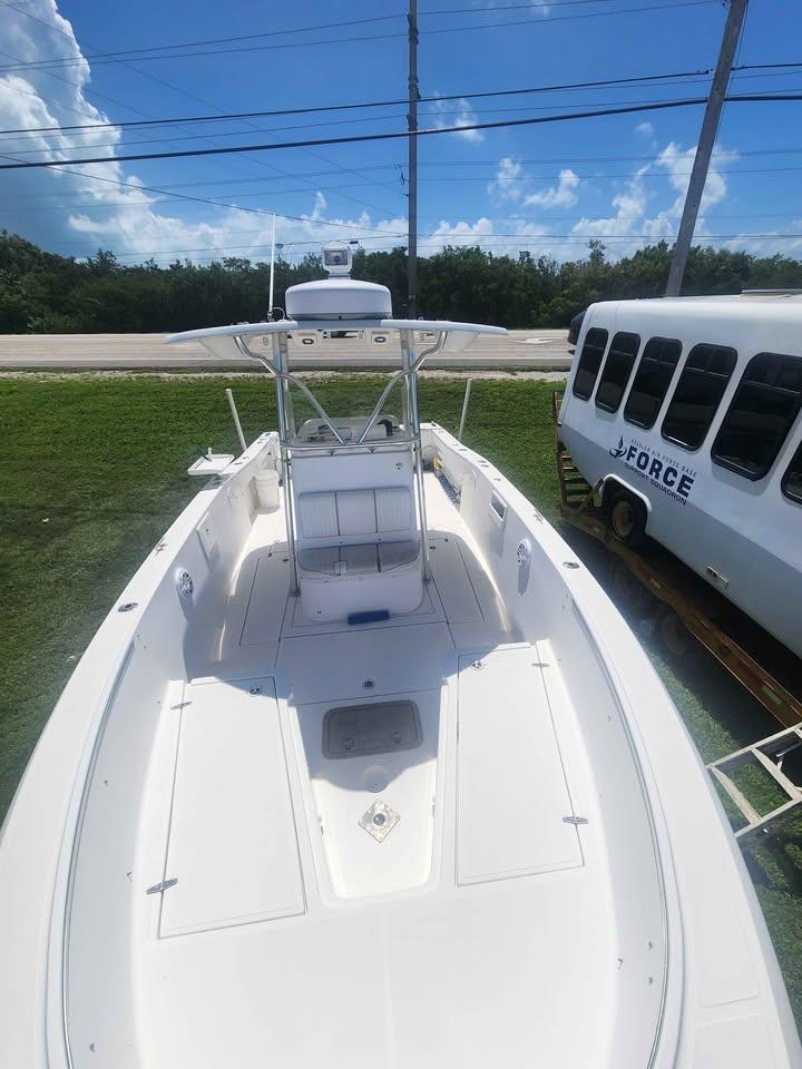 2006 Stamas 290 Tarpon boat with T-top, parked on grass near a white bus.