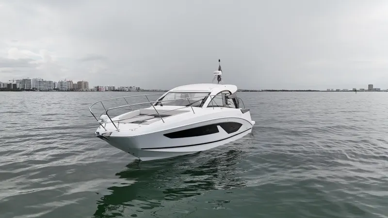  Yacht Photos Pics 2025 Beneteau Gran Turismo 36 yacht on calm waters, city skyline in background.