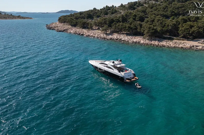  Yacht Photos Pics 2008 Sunseeker Predator 72 yacht anchored in clear blue waters near a rocky coastline.