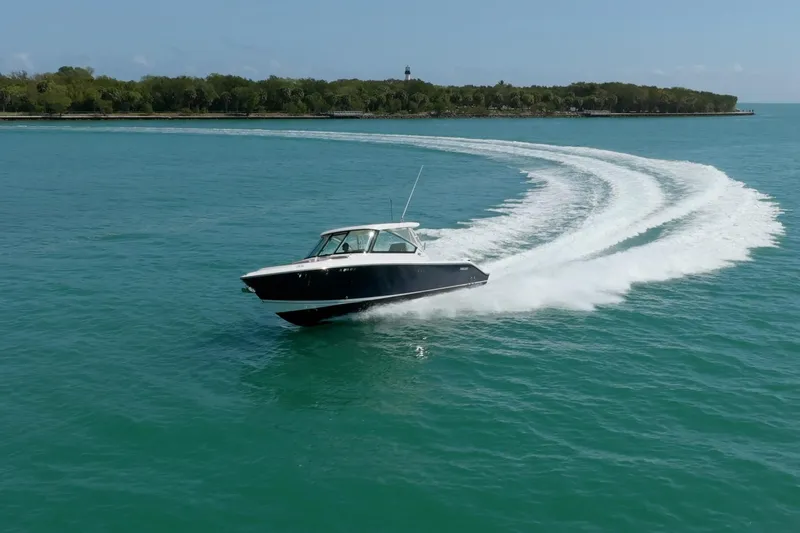 Waikiki Yacht Photos Pics 2017 Pursuit DC 325 Dual Console boat cruising on clear blue water near a lush island.