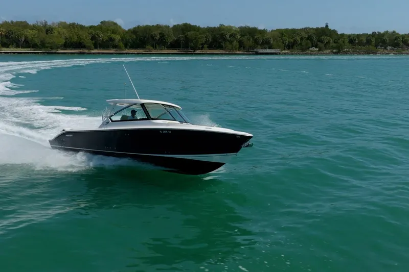 Waikiki Yacht Photos Pics 2017 Pursuit DC 325 Dual Console boat cruising on turquoise water near a forested shoreline.