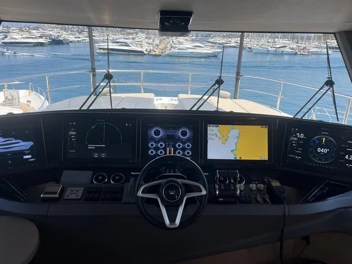  Yacht Photos Pics Control panel of 2023 Princess X80 yacht overlooking marina with multiple screens and steering wheel.