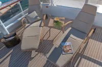 Two cushioned loungers on a yacht deck with a small table, magazine, and decorative items.