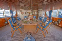 Luxurious yacht interior with striped chairs, round table, and wooden decor, 1982 Custom Displacement Twin Screw.