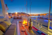 Luxurious yacht deck at sunset with candles, wine glasses, and cityscape view.