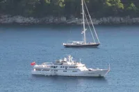 Luxury yacht and sailboat anchored in serene blue waters, surrounded by lush greenery.