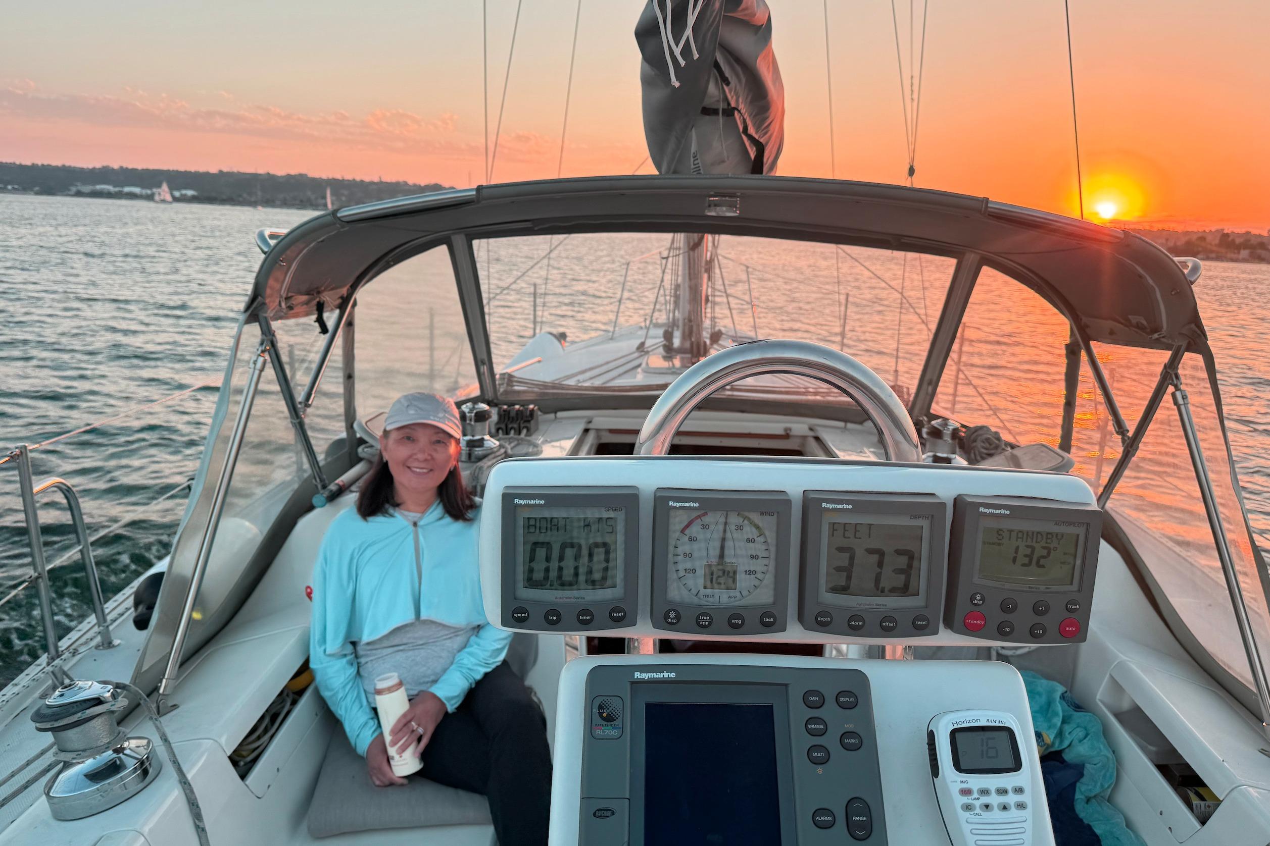 Woman enjoying sunset on a 2003 Catalina 34 MkII sailboat, with navigation instruments visible.