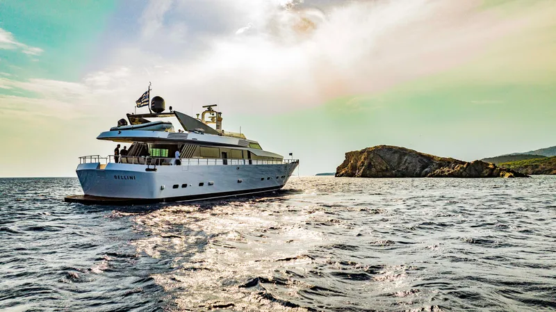 Bellini Yacht Photos Pics Luxury yacht Cantieri di Pisa AKHIR 30, 1988, cruising near rocky coastline under vibrant sky.
